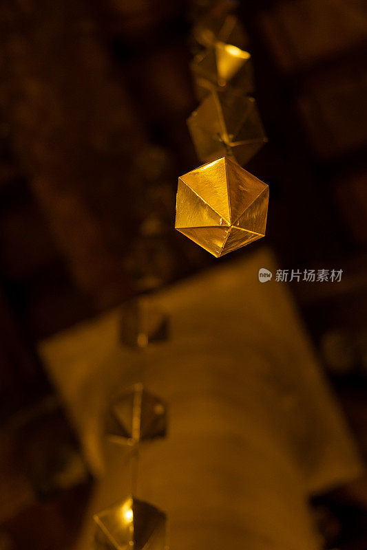 一颗金色钻石的低角度细节悬挂在granollers门廊的木质天花板上，随后是两颗以上的钻石。手机垂直比例视图。