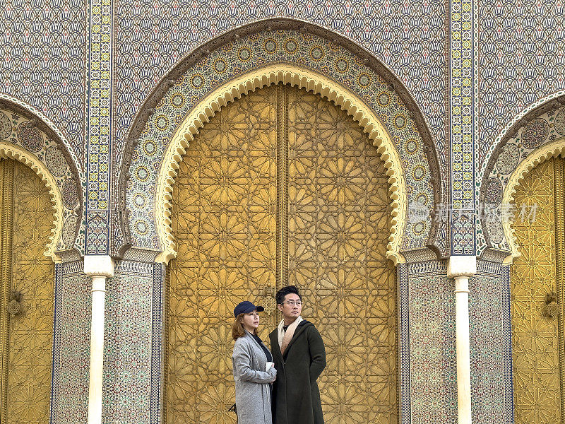 在摩洛哥菲斯，一对亚洲中国游客站在皇宫入口望向别处。