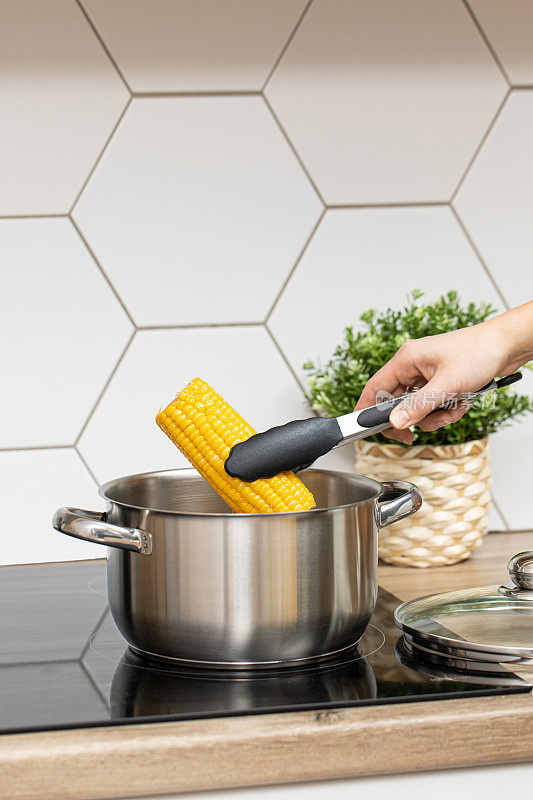 现代厨房用钳子从锅里煮玉米