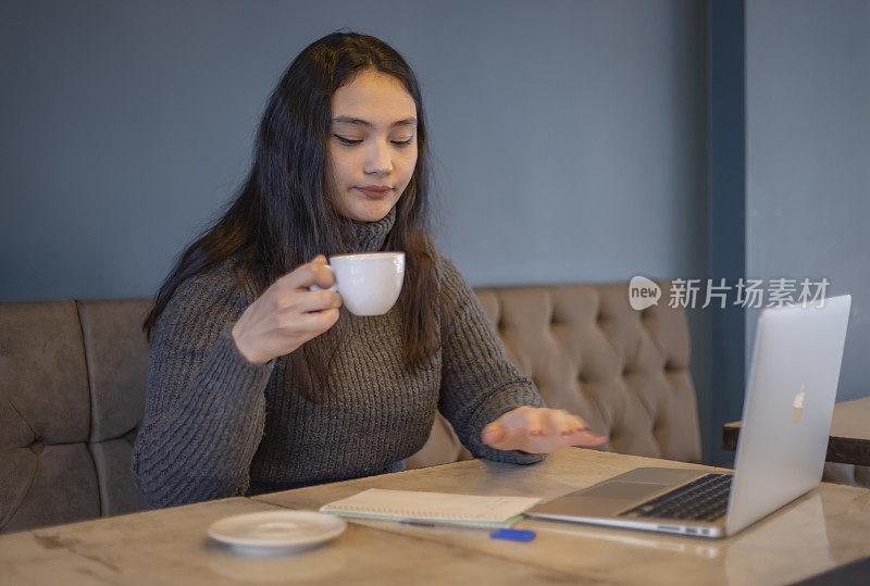 一名年轻的亚洲女子在咖啡馆边喝咖啡边摆弄电脑