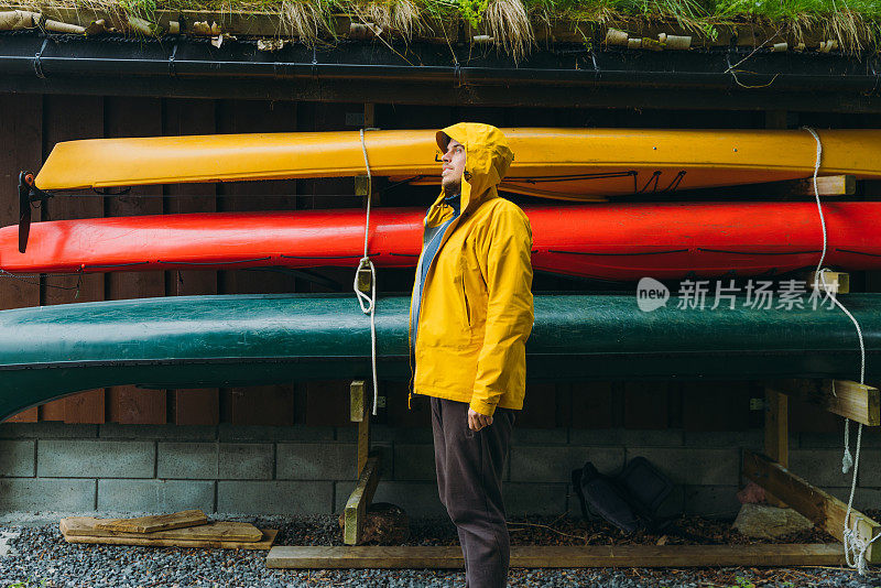 挪威，一名穿黄色夹克的男子带着一只狗和独木舟呆在房子旁边