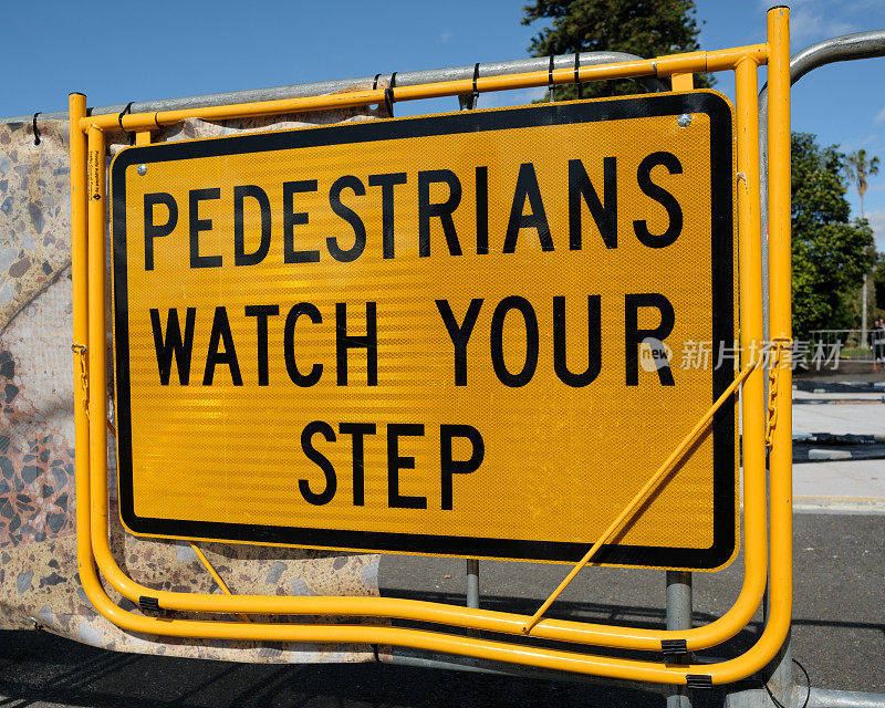 黄色金属步行街标志，提醒行人注意脚下
