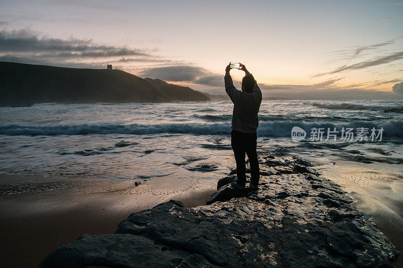 一个人在黄昏时给大海拍照