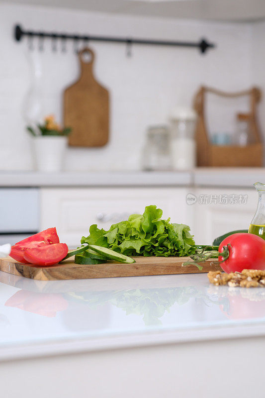 切新鲜的西红柿，黄瓜，蔬菜沙拉，坚果，油在餐桌上在一个明亮的厨房，特写