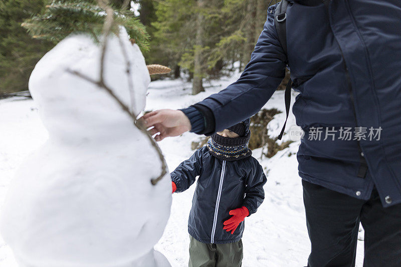 一个快乐的男孩和他的爸爸在森林里和白雪公主玩耍。他穿着一件深色夹克，戴着红色手套。冬天,下雪了。库存图片