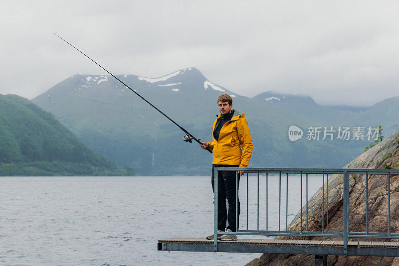 身穿黄夹克的男子在挪威峡湾边钓鱼