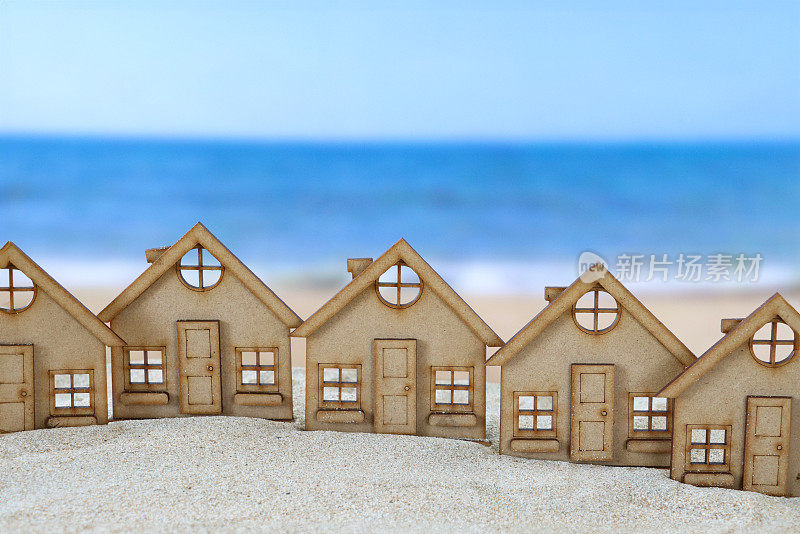 在一堆沙子上的一排木制镂空模型度假小屋的特写图像，沙滩背景与退潮时的波浪，大海和海岸线，重点放在前景，度假租赁和度假屋的概念