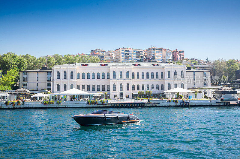 夏天，土耳其伊斯坦布尔博斯普鲁斯海峡的全景，一艘小游艇在海上豪华的奥斯曼宫殿前摆姿势。