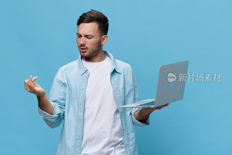 一个穿着休闲基本款t恤、皮肤黝黑、神情凝重的英俊男子，用手指数着数着，手里拿着笔记本电脑，在蓝色的工作室背景下独自摆姿势。复制空间横幅模型。电子维修IT概念