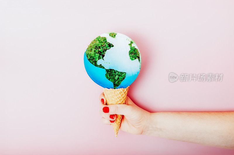 女性手持华夫蛋筒，以地球模型为冰淇淋甜点，粉色背景。暖化、臭氧空洞、融化、污染或气候变化的概念。拯救地球，地球日的概念。