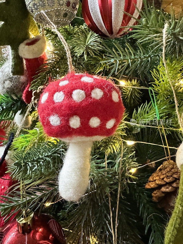 自制的特写图片，毛毡毒菌装饰挂在人造圣诞树的树枝上，云杉针，模糊的白色仙女灯的背景