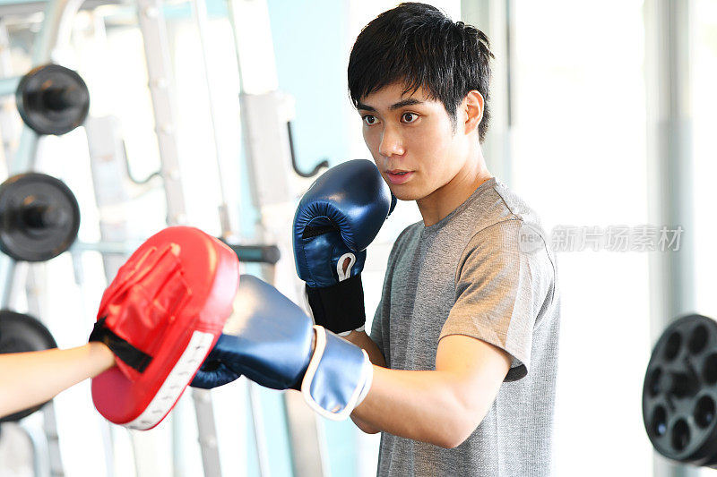 亚洲男子在武术馆出拳，教练手握出拳手套