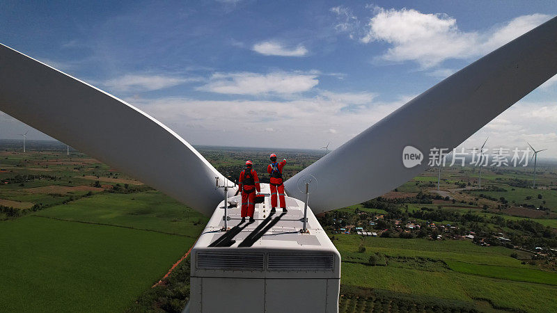 风力涡轮机农场，穿着红色安全制服的风力涡轮机技术人员和工程师在风车上工作