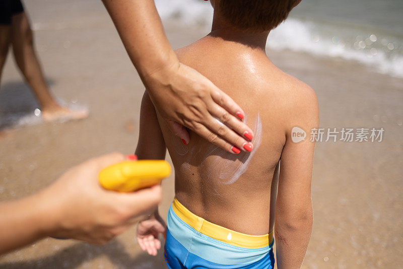 在沙滩上，母亲正在给儿子的背上涂防晒霜