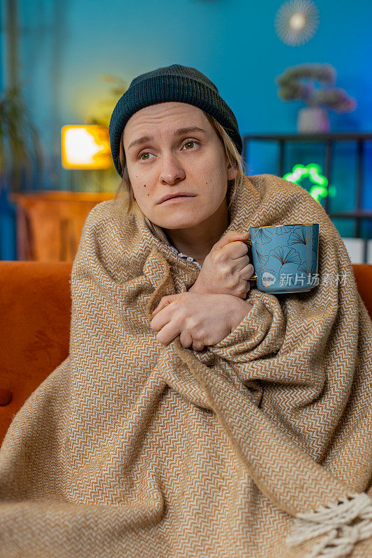 生病的不健康的女人冻僵了，感觉很糟糕，盖着温暖的毯子在家里喝茶