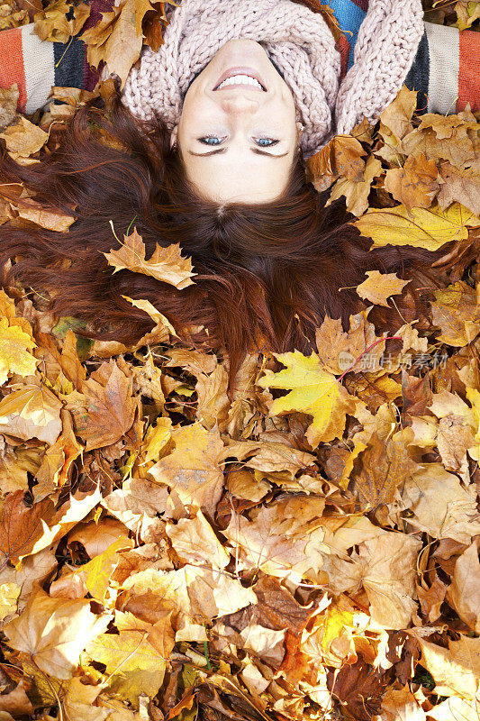 一个红头发的女人躺在秋叶上。