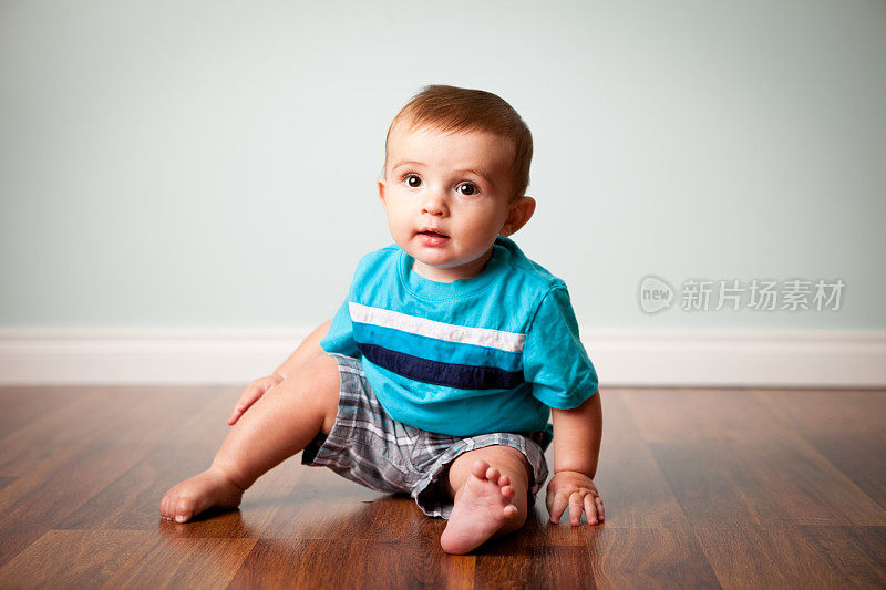 微笑的小男孩坐在木地板上的彩色图像