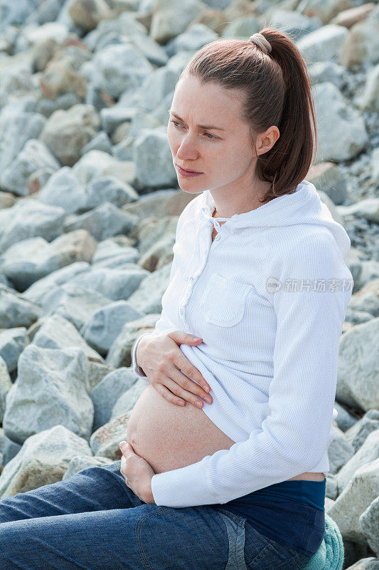 悲伤的孕妇独自坐在石头海滩上