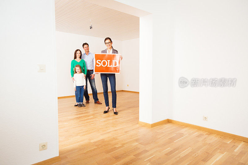 房地产经纪人在空荡荡的公寓里，举着“售出”的牌子