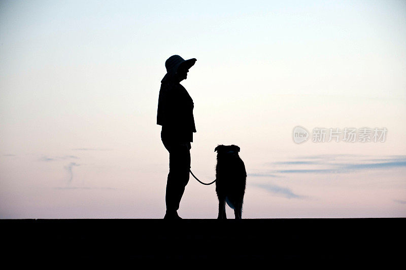 成熟的西班牙妇女和牧羊犬剪影日落