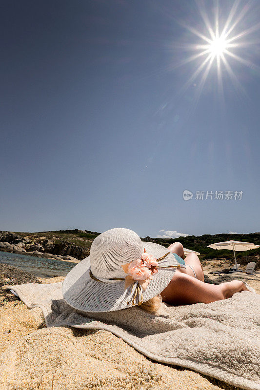 一个戴着太阳帽的陌生女人在海滩上晒日光浴。