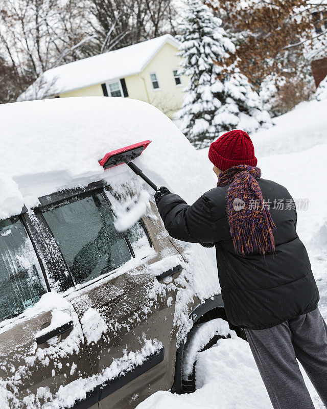 冬季女人刮掉汽车上的厚厚的积雪