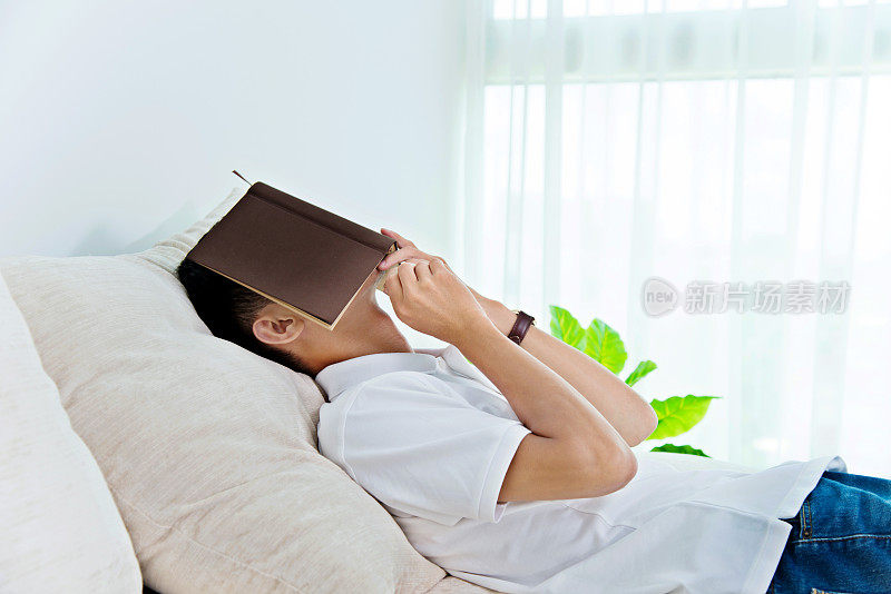 年轻人睡在沙发上，脸被书遮住了