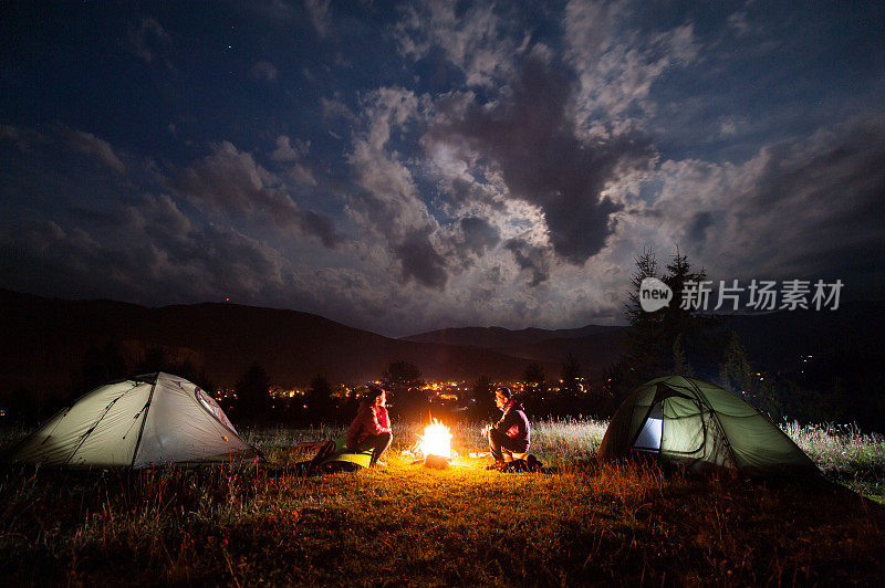 女孩和男孩晚上坐在帐篷附近的篝火旁
