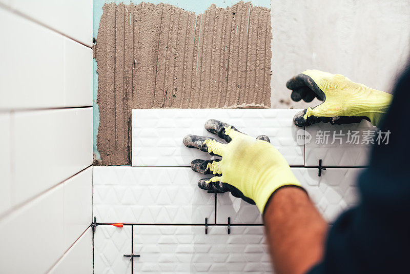 建筑工人在浴室墙壁上安装小瓷砖，并用镘抹砂浆
