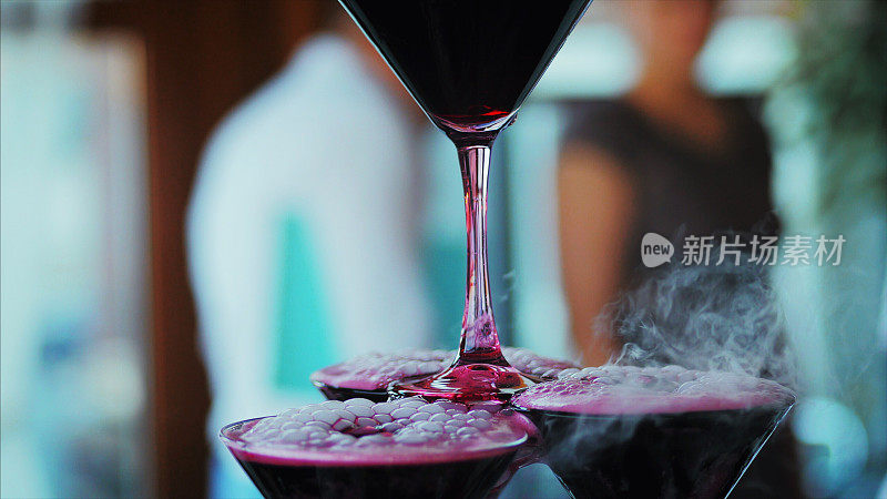 侍者将红酒或香槟酒倒入装有液氮的玻璃杯中。年轻人把酒杯里的酒倒进金字塔里
