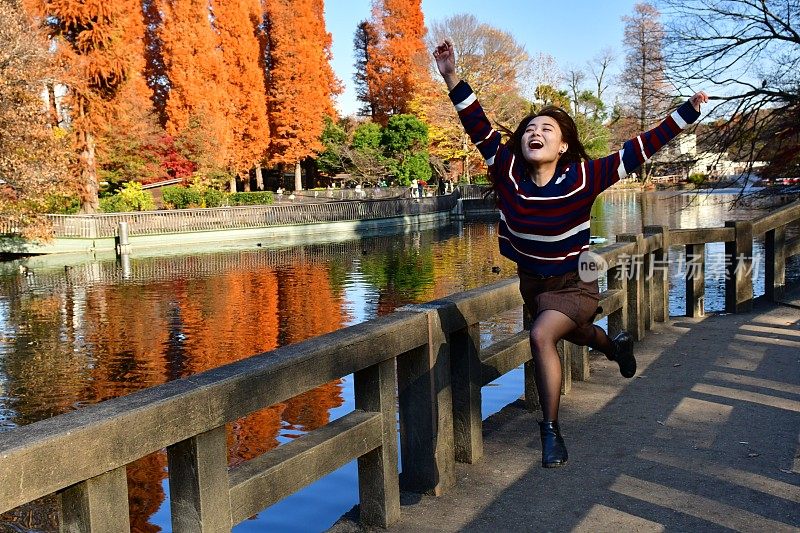 年轻的日本女子在东京的猪城公园的桥上跑和跳