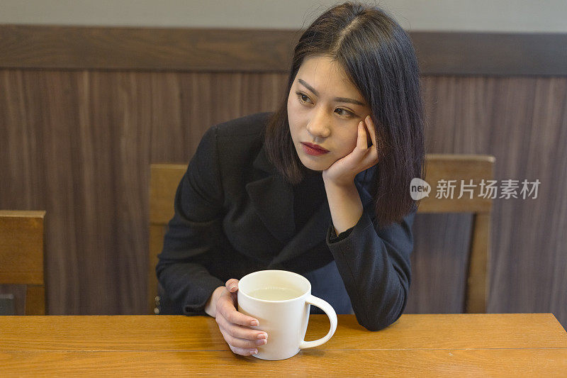 一个沉思的女人在咖啡馆拿着一杯咖啡的肖像