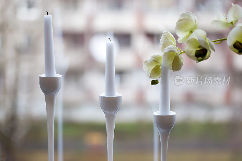 三支白色蜡烛插在优雅的烛台上，上面插着兰花花
