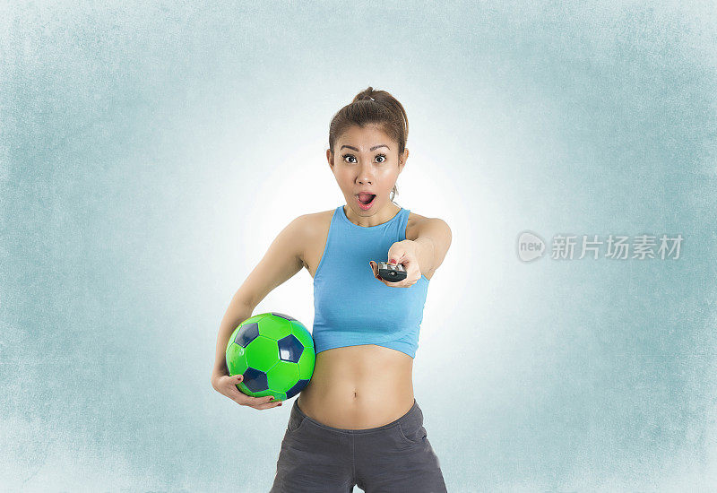 女子足球运动员将电视遥控器指向蓝色背景