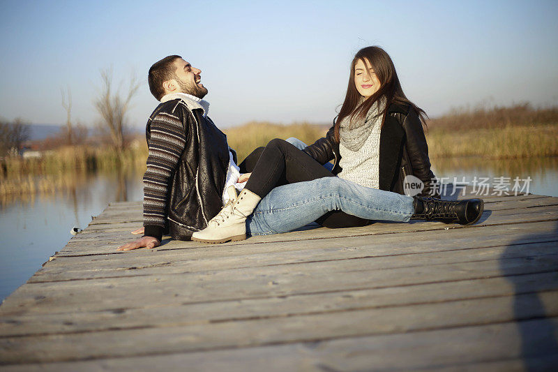 一对漂亮的夫妇坐在湖边的码头上
