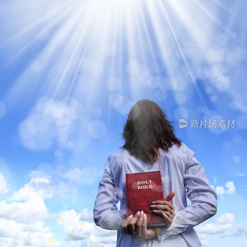 一名年轻女子在一束光前，手里拿着《圣经》