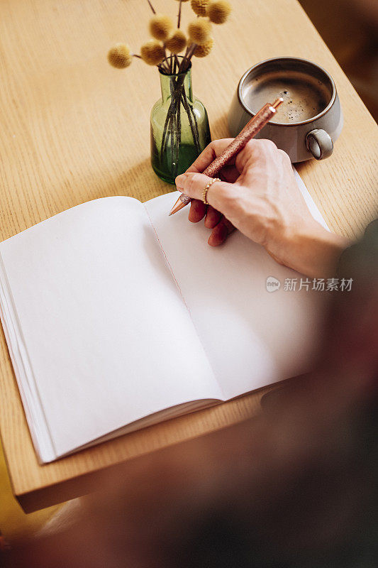 女人在笔记本的空白页上写字，喝着咖啡