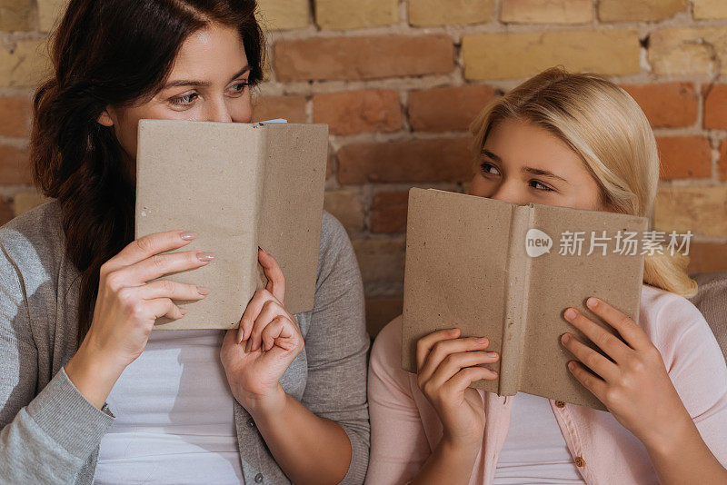 母亲和女儿在家里用书本遮住脸