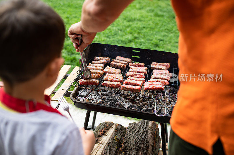 一个小男孩看着他的爷爷烤肉