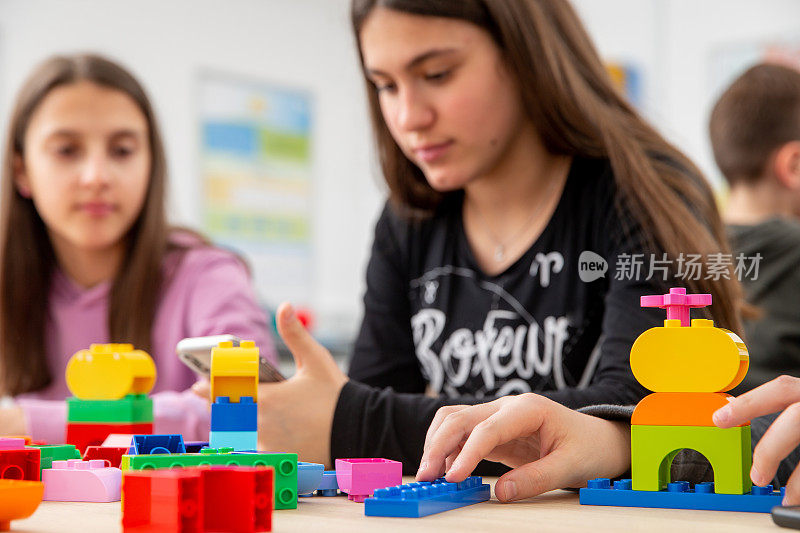 十几岁的女孩坐在教室与玩具积木，如果在她前面使用移动设备-库存照片