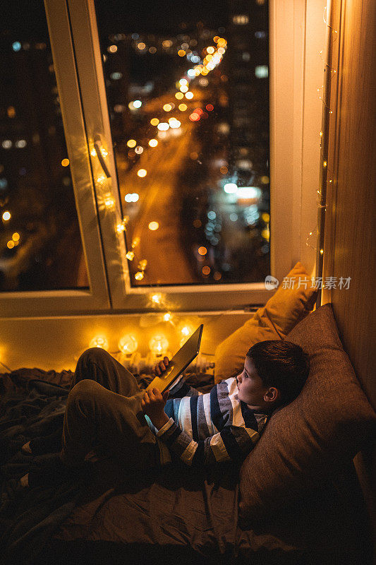 可爱的小男孩躺在床上，在平板电脑上看书