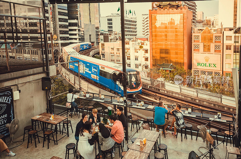 人们在带有城市景观和移动的地铁的露天餐厅喝啤酒
