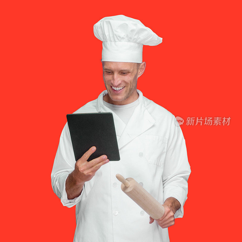 白人年轻男厨师在有色背景下穿着裤子，使用触摸屏