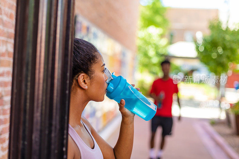 千禧年男性和Z一代女性在炎热的夏日里锻炼，拿着水瓶补水