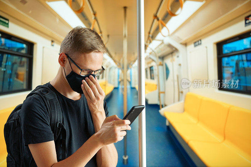 地铁里的一名男子正在调整他的面具，眼睛一直盯着手机屏幕