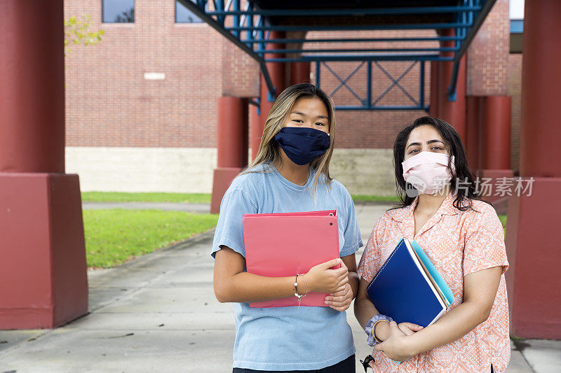 各种各样的女性戴着口罩站在学校外面