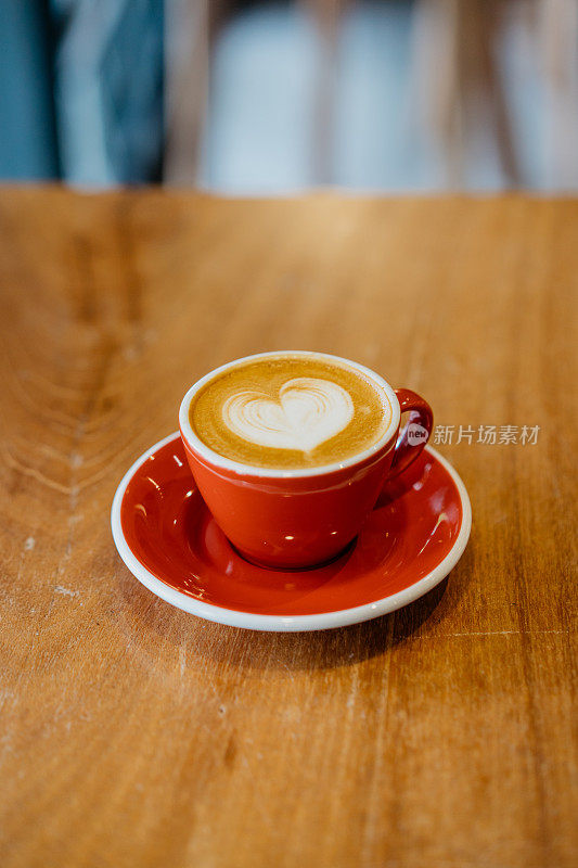 木桌上的红色咖啡杯上有泡沫的拿铁咖啡