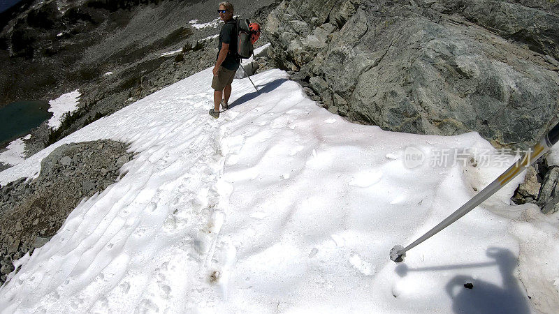 徒步旅行者沿着白雪和岩石覆盖的山坡行走