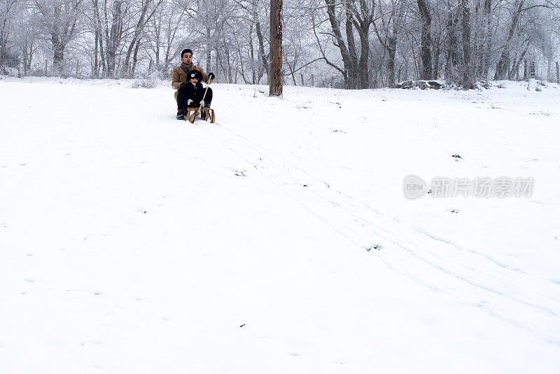 一对父子驾着雪橇走下白雪覆盖的草地