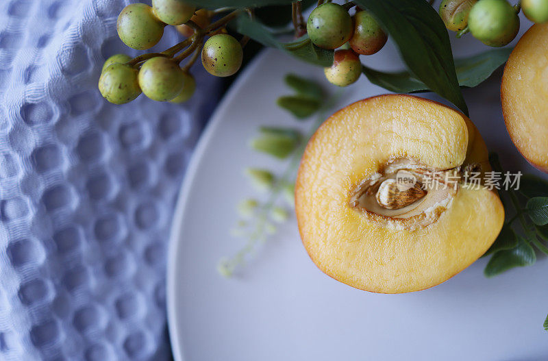 灰色盘子上放着半个桃子，淡紫色的亚麻餐巾和缀着浆果的树枝